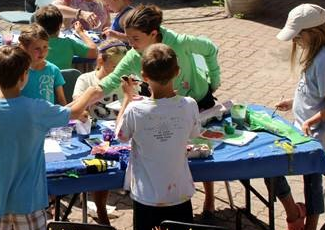 children gather around a table outside to do crafts